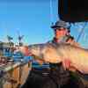 Spencer Bauer holds up a hefty blue catfish aboard his boat on a sunny winter day.